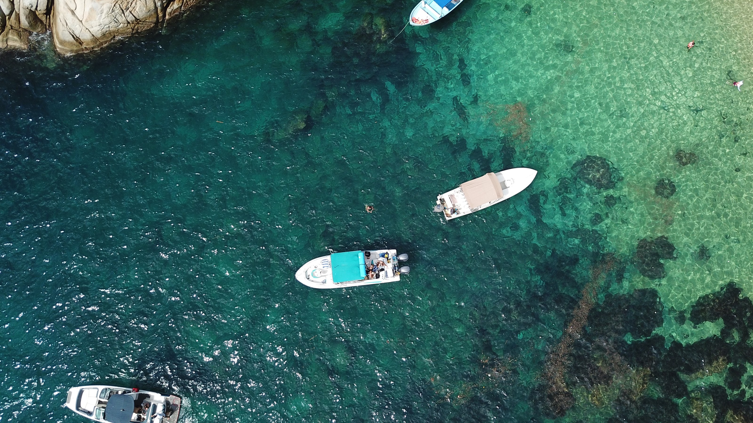 Una playa vista desde arriba: agua profunda, arrecife, arena y una lancha anclada.