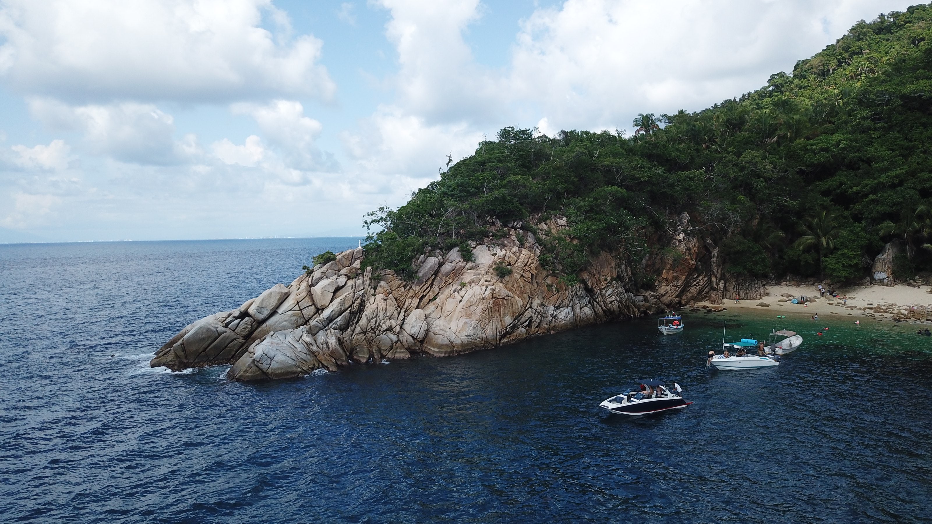 Una punta rocosa cubierta de selva, vista desde el agua, con el mar en calma alrededor.